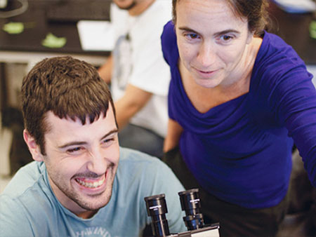A student using a microscope and being shown something by his professor.